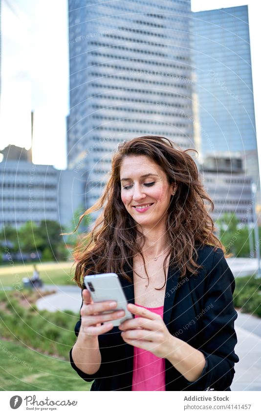 Cheerful businesswoman in jacket browsing smartphone on street entrepreneur using city classy smile urban female mobile device gadget communicate internet
