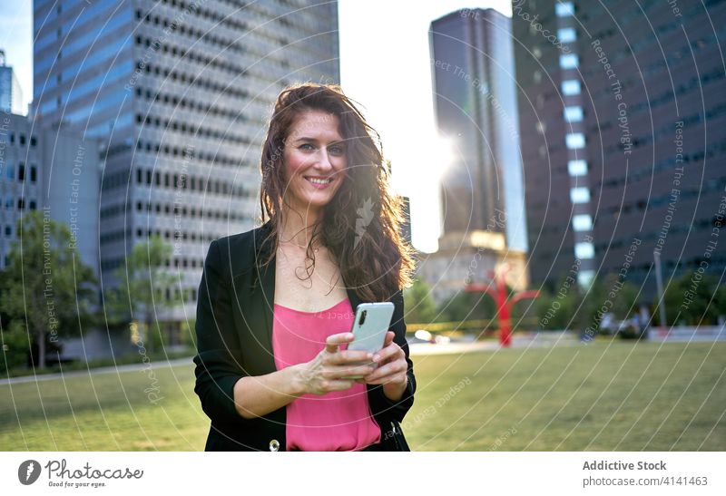 Cheerful businesswoman in jacket browsing smartphone on street entrepreneur using city classy smile urban female mobile device gadget communicate internet