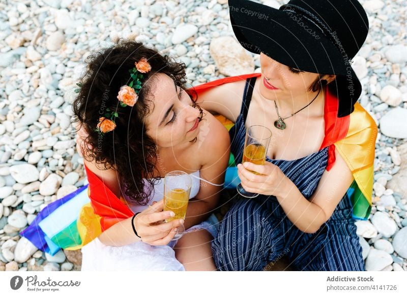 Happy homosexual women hugging and drinking beverages lesbian couple champagne lgbt flag beach clink rainbow tolerance equal together tender embrace romantic