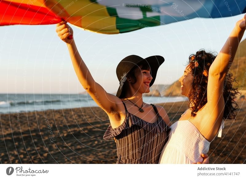 Happy women raising multicolored flag standing on sea beach pride girlfriend lgbt lesbian vacation ocean freedom weekend homosexual same sex together shore