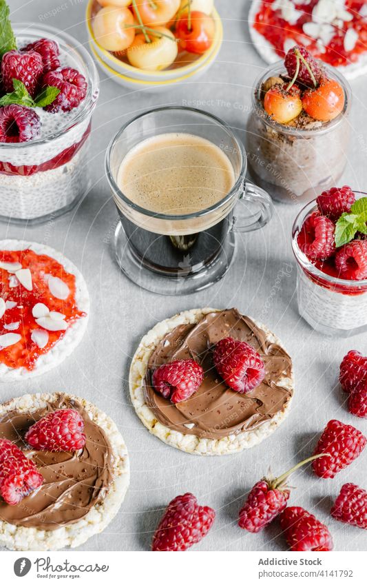 Chia puddings served with crispbreads and coffee breakfast berry jam cherry raspberry slice nut chia sweet spread peanut butter almond flake glass cup food