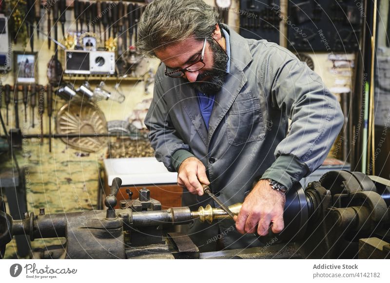 Crop concentrated goldsmith using sharpening machine in workshop craftsman handicraft metal stick process uniform small business profession artisan jeweler job