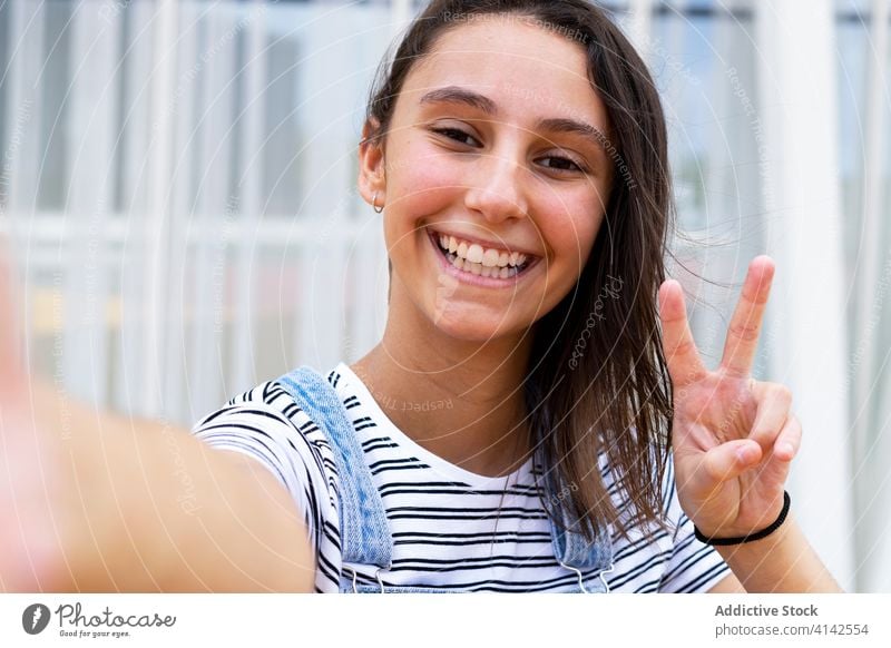 Cheerful teenager gesturing V sign and taking selfie v sign smile street city weekend modern rest cheerful happy gesture joy girl adolescent casual glad