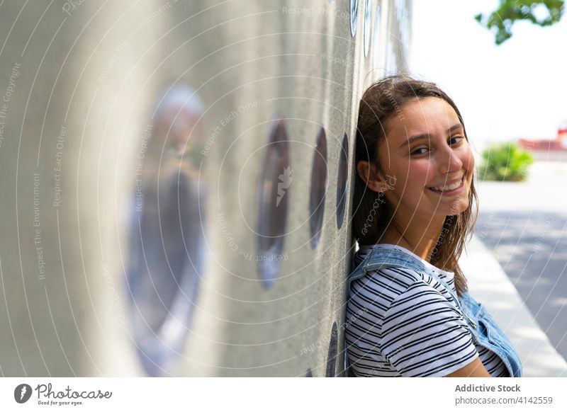 Cheerful teenager leaning on wall smile rest street city casual happy joy urban sunny daytime adolescent cheerful relax positive modern trendy glad town