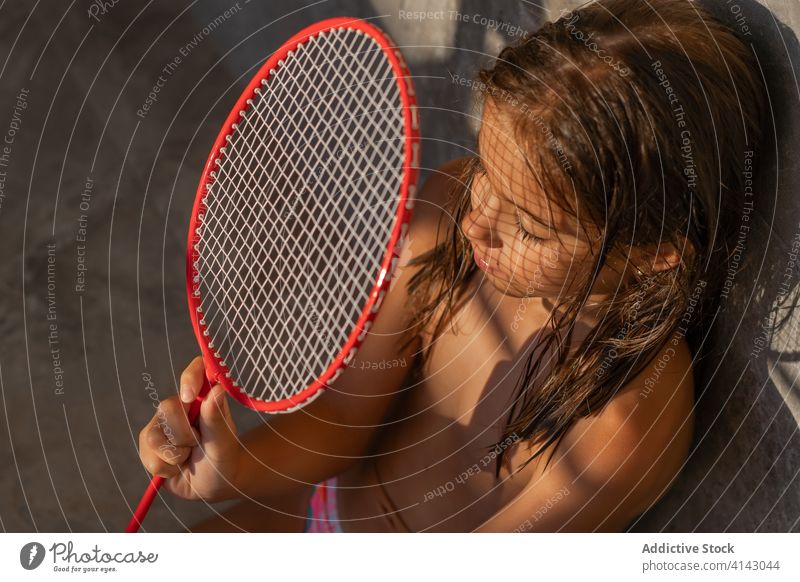Child with badminton racket in courtyard shadow child sunlight backyard sunny kid calm equipment sit relax daytime rest weekend summer tranquil serene adorable