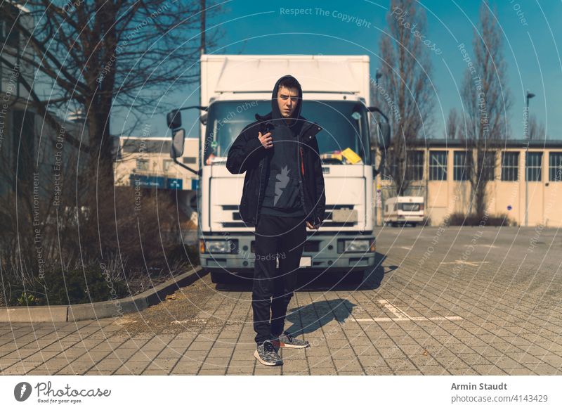 young man with backpack stands in front of a truck aeria architecture beautiful black boy building casual caucasian confident hoodie lifestyle looking lorry