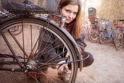 Young woman pumps up the tires of her bike activity air bicycle casual caucasian closeup confident crouching details equipment female fix girl lifestyle macro