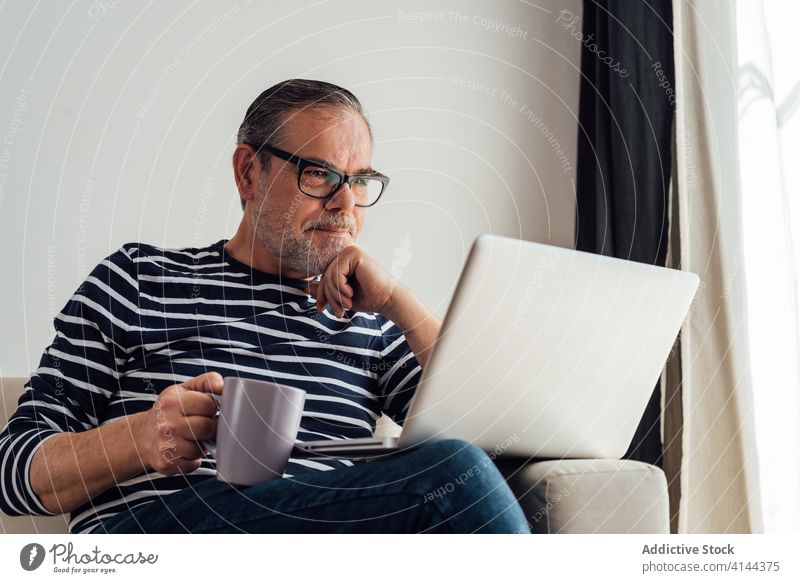 Adult man drinking coffee and using laptop copy space confident technology caucasian work covid19 couch communication coronavirus one modern indoors thoughtful
