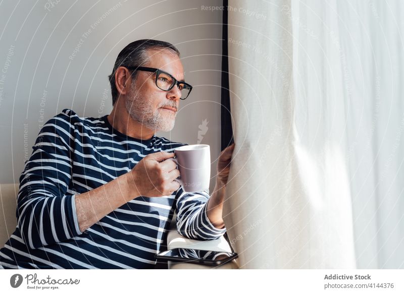 Bearded guy with hot drink looking out the windows man balcony morning rest casual home apartment male beard lifestyle beverage coffee tea tranquil serene