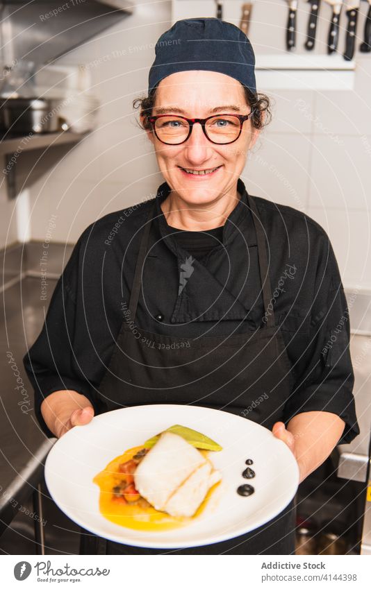 Portrait of a female chef holding a cod dish. portrait fish food restaurant gourmet plate sea hat catering character platter dinner cook cap happy delicious