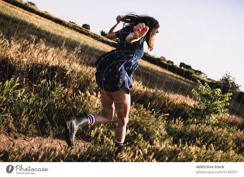 Cheerful woman running along field countryside carefree weekend summer sunny freedom cheerful female rubber boot dress joy meadow nature harmony idyllic grass
