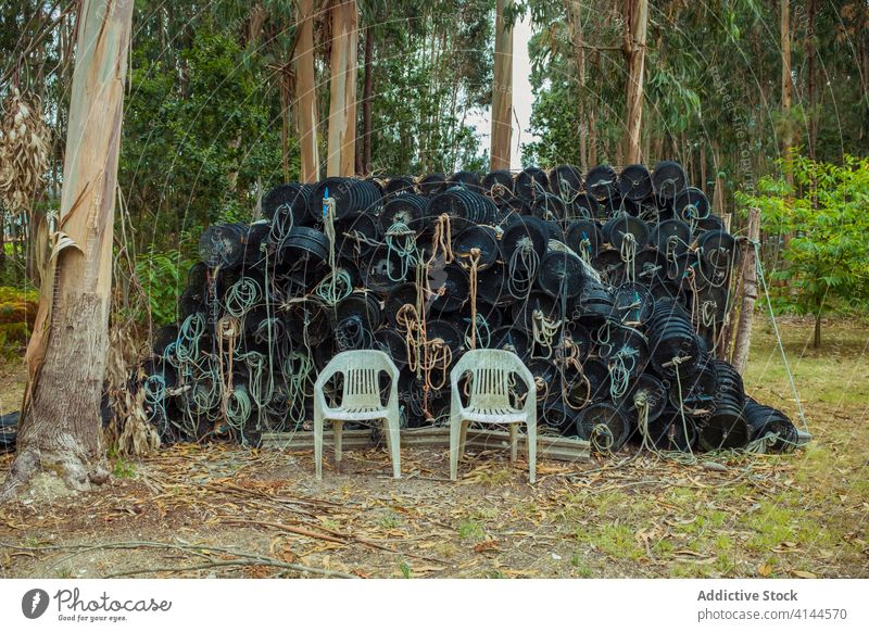 Pile of fishing equipment and chairs near growing trees stool rope pile empty trunk solitude dirty quiet idyllic nature scenery old harmony natural abandoned