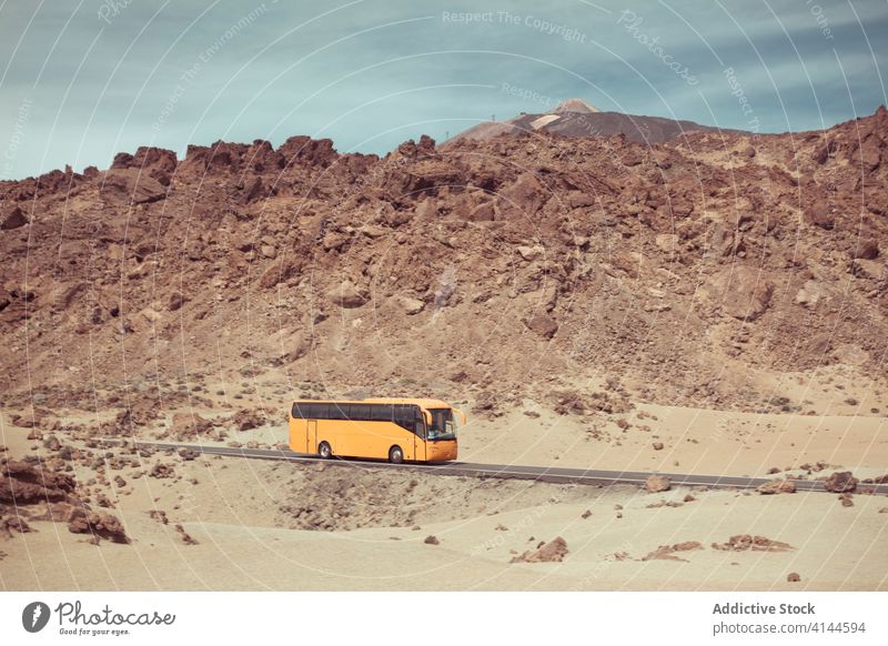 Colorful bus driving on road of dry rocky terrain in daylight mountain desert stone colorful sky highland sandy drive nature picturesque idyllic cloudy harmony