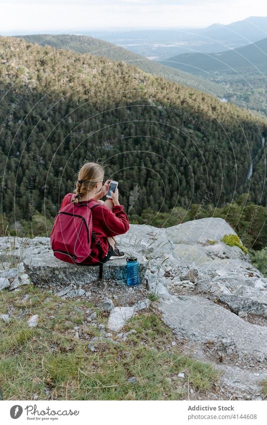 Female backpacker using smartphone while resting on mountain top woman hike travel activity trekking browsing check forest stone young nature adventure spain
