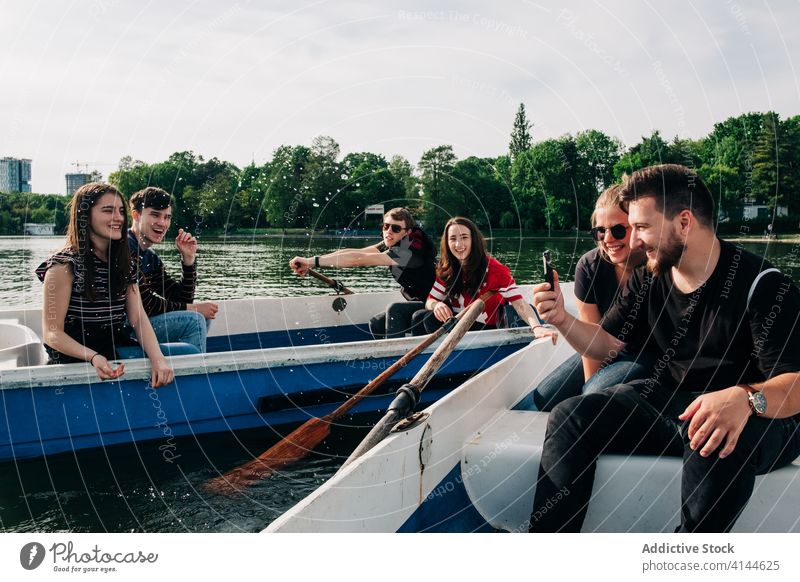 Happy friends having fun on boats and using smartphone pond laugh happy positive nature friendship activity picturesque browsing young chill cheerful carefree