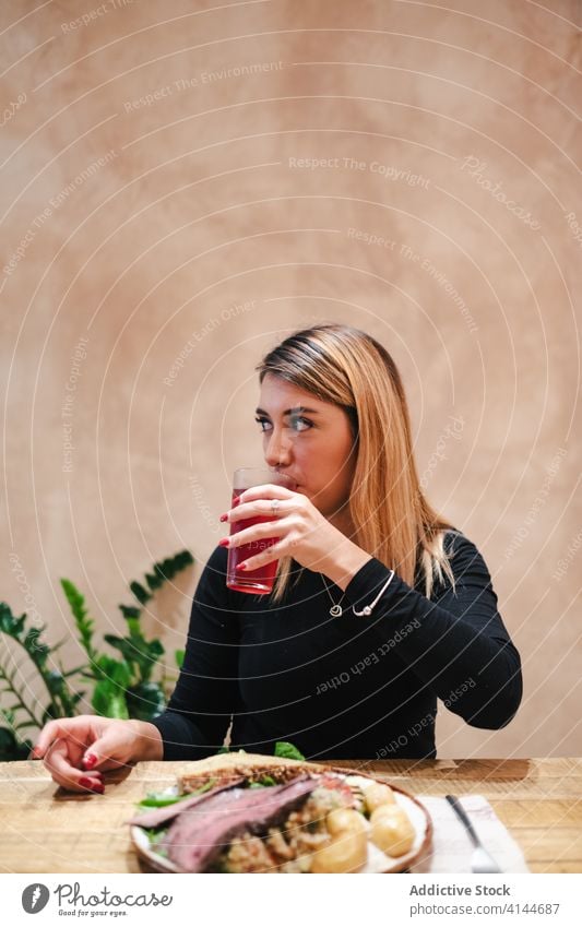 Content woman drinking juice and sitting at table in cafe tasty beef yummy beverage dine positive lunch meal eat dinner cuisine gourmet restaurant refreshment