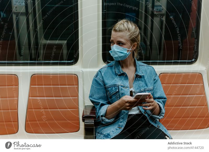 Young woman in protective mask using smartphone in subway train coronavirus passenger metro social distancing covid pandemic browsing restriction infection