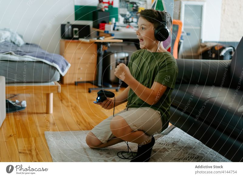Cheerful child having fun while playing video game at home boy celebrate headphones joystick victory excited cheerful entertain device happy kid little casual