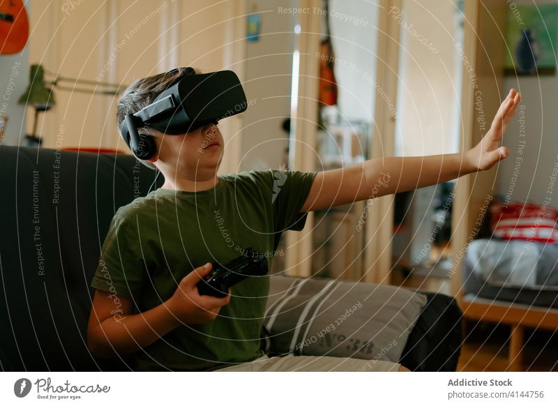 Child in VR headset playing on couch boy vr goggles gamepad virtual reality using sofa entertain modern home device child kid little adorable gadget childhood