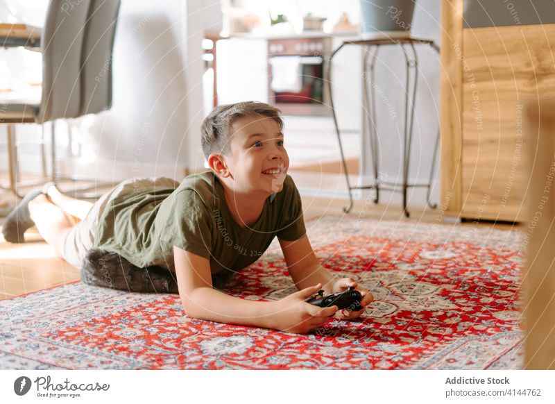 Cute child lying on carpet at home and playing on console boy video game floor joystick hobby free time leisure device gadget concentrate entertain childhood