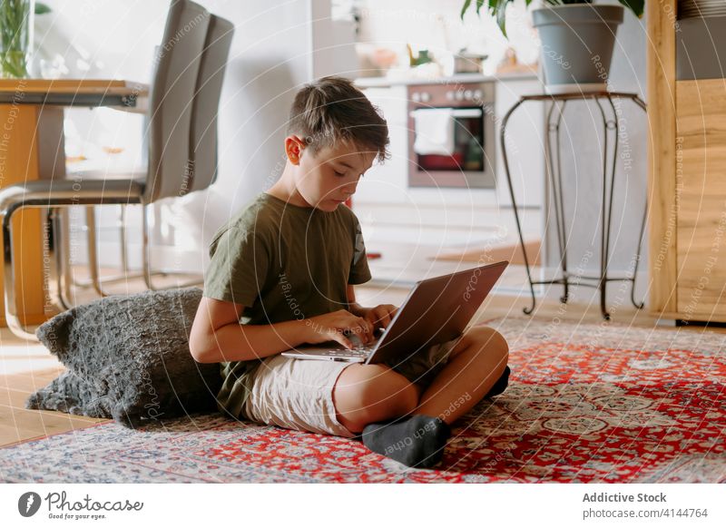 Focused kid using laptop at home boy typing floor internet serious legs crossed device gadget browsing online connection child little casual childhood smart