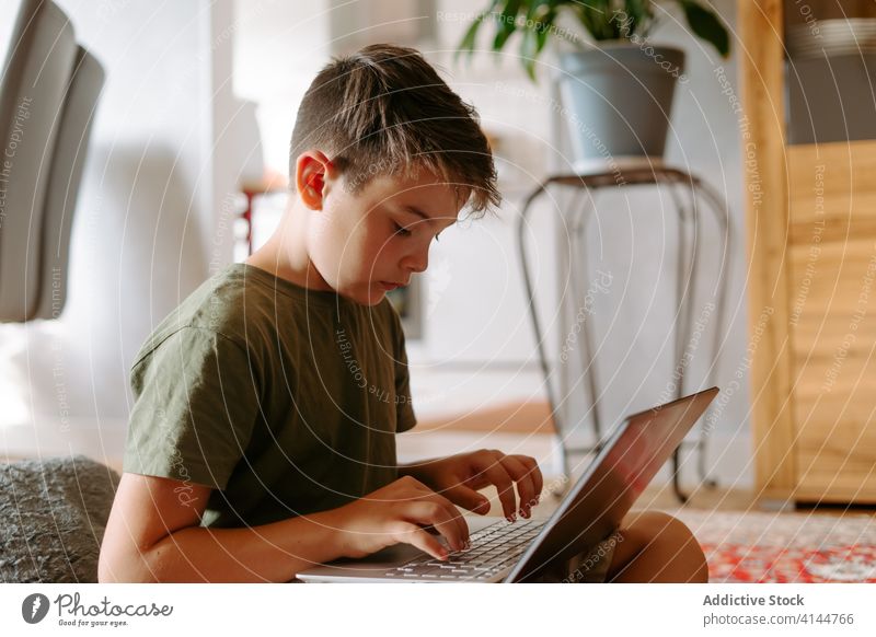 Focused kid using laptop at home boy typing floor internet serious legs crossed device gadget browsing online connection child little casual childhood smart