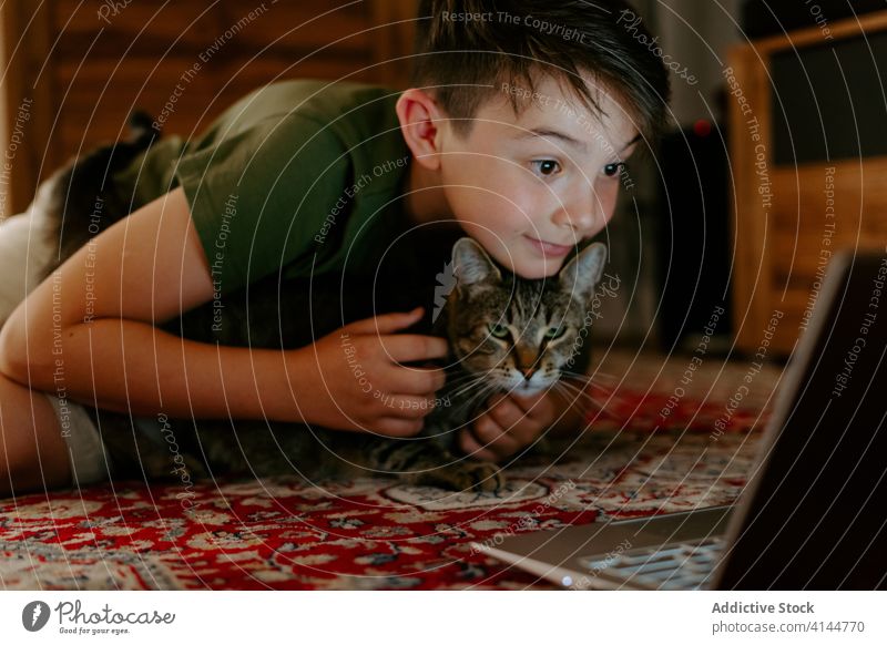 Little boy and cat resting on floor with laptop kid cuddle video having fun cheerful excited happy point together adorable watch device using internet gadget