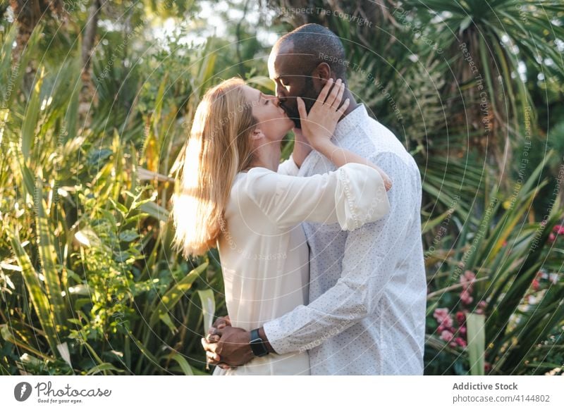 Romantic diverse couple kissing passionately in evening garden tender romantic content hug eyes closed sunset love affection embrace bonding modern casual