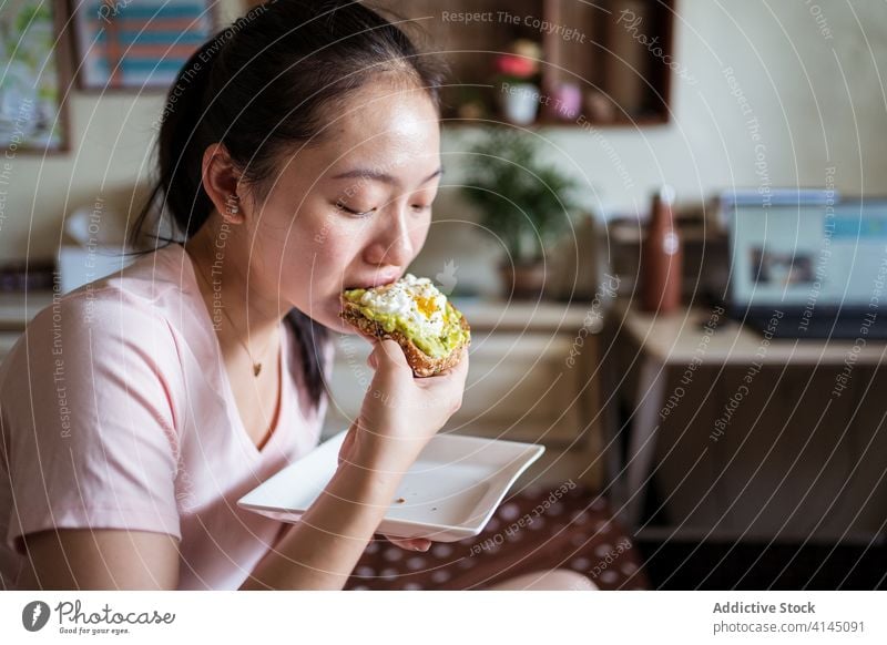 Ethnic woman eating breakfast on bed toast avocado egg delicious healthy nutrition morning female ethnic asian cozy home food relax comfort tasty meal fresh