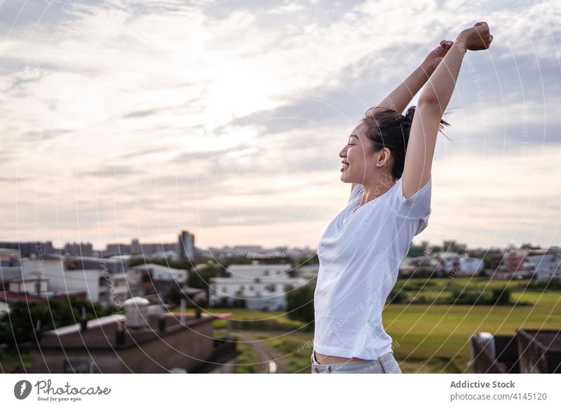 Happy Asian woman stretching body in morning smile happy arms raised sky cloudy sunrise terrace female young ethnic asian delight relax joy healthy optimist