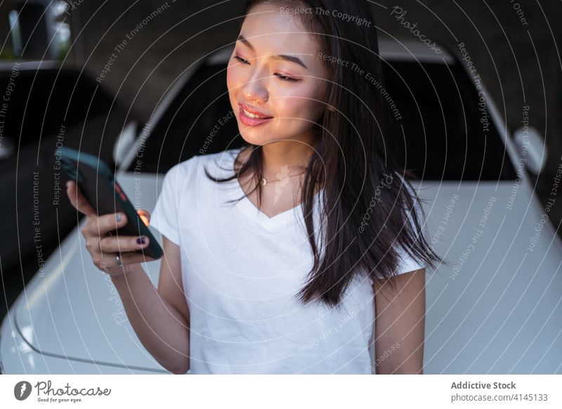 Happy Asian woman browsing smartphone near car using garage smile dark social media text message addict female ethnic asian vehicle device gadget happy joy
