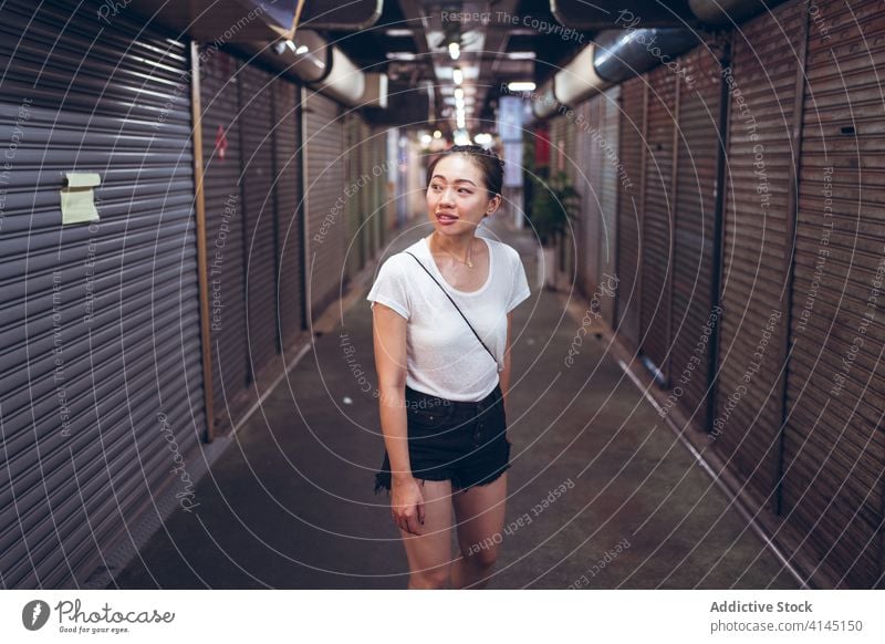 Young ethnic woman standing in underground corridor passage close shutter urban shop commerce announce read young asian female lifestyle modern contemporary