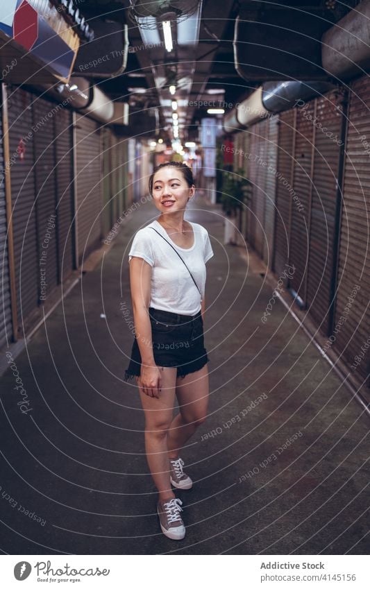 Young ethnic woman standing in underground corridor passage close shutter urban shop commerce announce read young asian female lifestyle modern contemporary