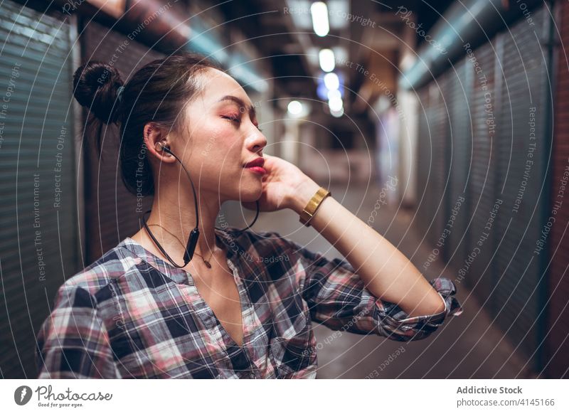 Woman with headset standing in underground corridor woman communicate talk casual urban asian ethnic millennial joy conversation lifestyle modern discuss fun