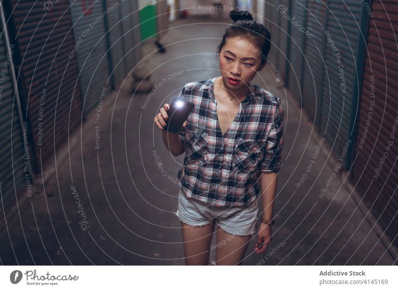 Young woman with flashlight walking in underground hall caution dark corridor passage narrow young asian female ethnic wary illuminate lifestyle way alone lamp