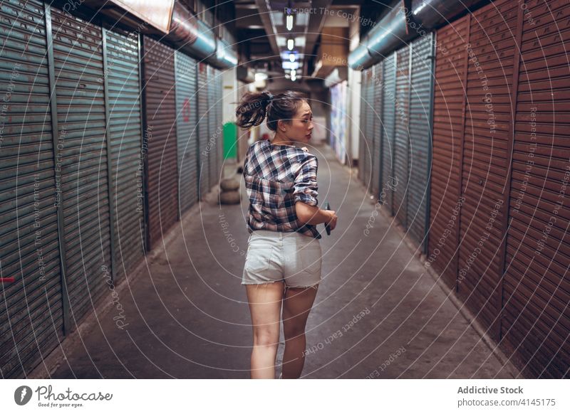 Young woman running on underground passage grunge scare smartphone corridor rush hall casual hurry alone move motion public close urban shutter young asian