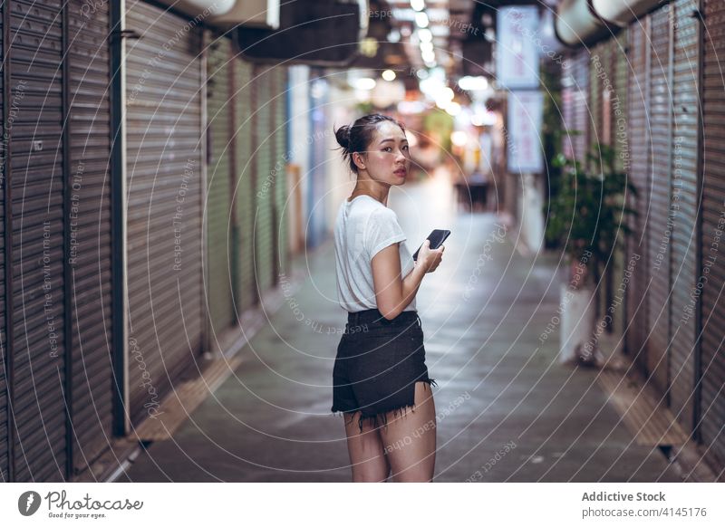 Ethnic woman with smartphone walking on underground passage city pedestrian public close urban shutter commerce young asian female ethnic mobile device gadget