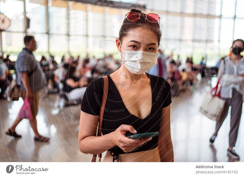 Asian woman using smartphone in modern airport departure lounge mask protect crowd coronavirus female ethnic asian contemporary internet mobile surfing people