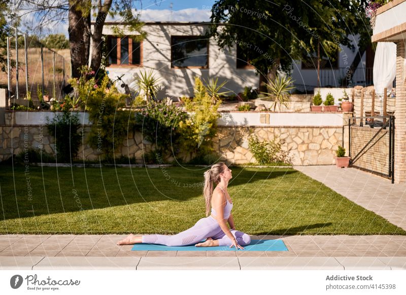 Flexible woman practicing yoga in Pigeon posture pigeon pose practice meditate backyard flexible asana ardha kapotasana female poolside mat serene relax harmony