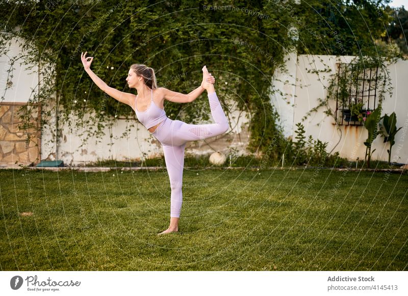 Graceful woman doing yoga in Lord of the Dance pose lord of the dance pose natarajasana flexible grace sportswear lawn park tranquil female mudra gesture green
