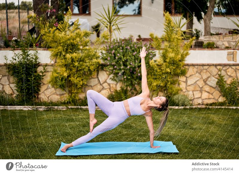 Concentrated woman doing yoga in Side Plank pose side plank vasisthasana flexible balance concentrate summer active wear female practice barefoot mat courtyard