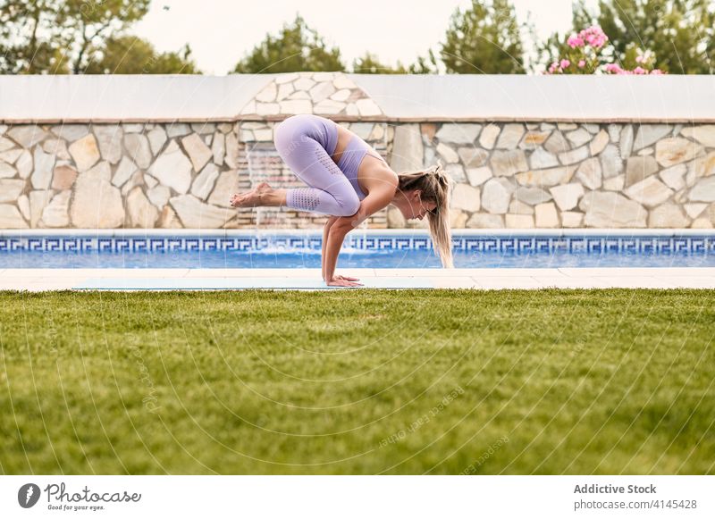 Flexible woman doing yoga in Crane pose crane pose bakasana balance practice poolside focus female active wear mat wellness summer healthy barefoot exercise