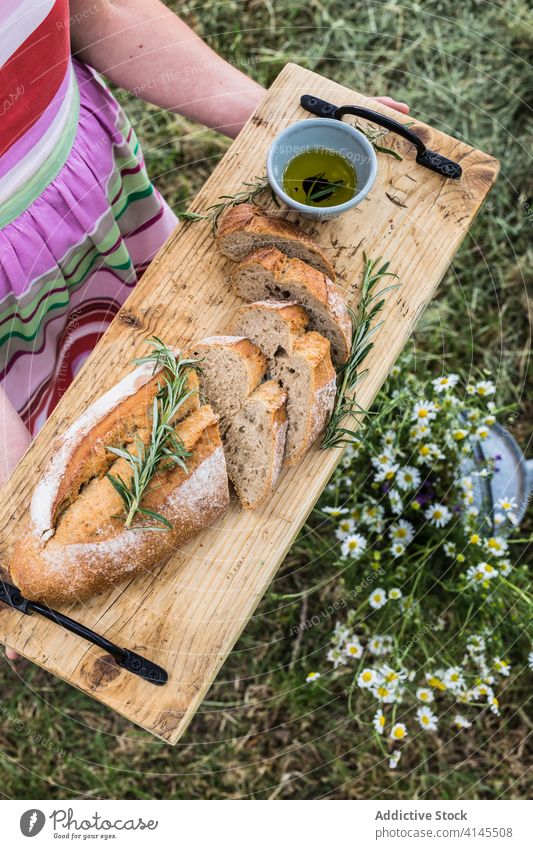 Crop anonymous woman serving appetizing bread with rosemary sprigs outdoors serve cutting board soft olive oil homemade healthy organic fresh herb savory grass