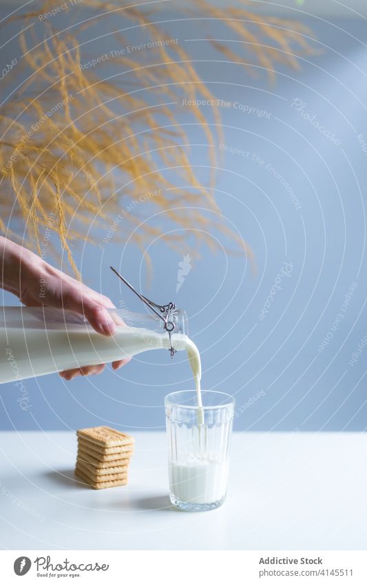Faceless person pouring milk into glass near biscuits at home bottle healthy dairy protein branch product transparent fresh pile cracker breakfast nutrient heap