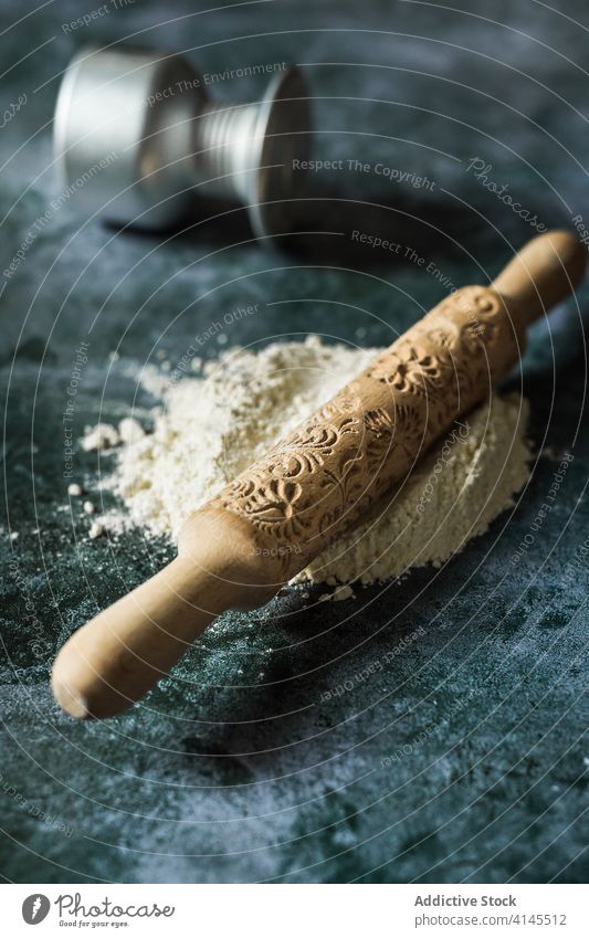 Wooden rolling pin with ornament on flour in kitchen floral culinary ingredient raw bowl natural product petal utensil dry decor loose texture organic uneven