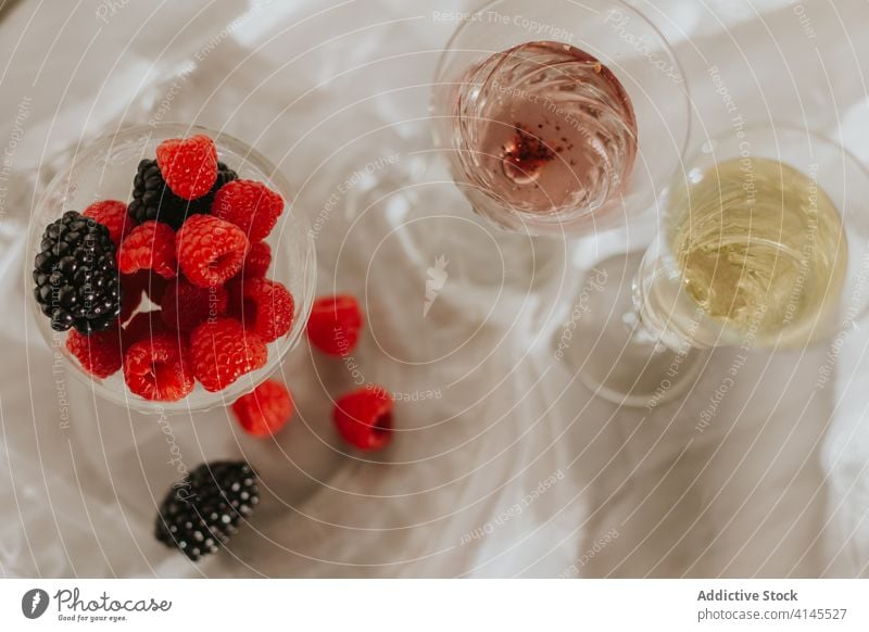 Glass of cocktail with berries and glasses served on table against white wall bottle plate berry drink composition decoration design creative elegant style