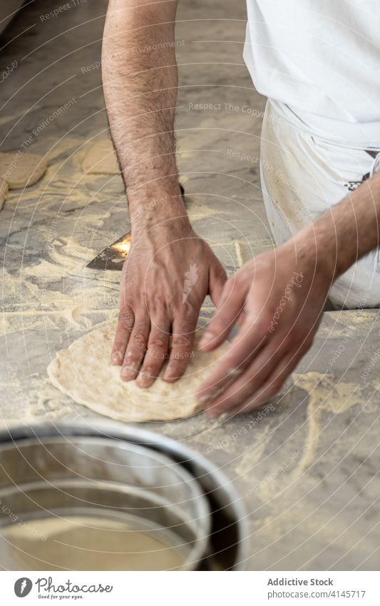 Crop pizzaiolo shaping pizza dough into circle in kitchen chef form round shape cook prepare knead male process culinary food italian cuisine professional