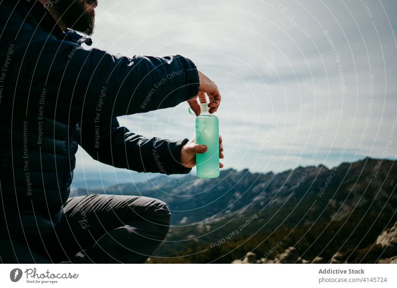 Anonymous male traveler drinking water in mountains man smile rest boulder puerto de la morcuera spain cheerful fresh bottle overcast sky vacation lifestyle sit