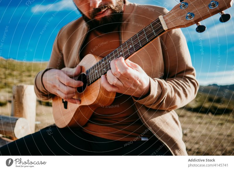 Bearded man playing ukulele in countryside fence sky cloudy music puerto de la morcuera spain male travel serious vacation trip nature rest journey sunny