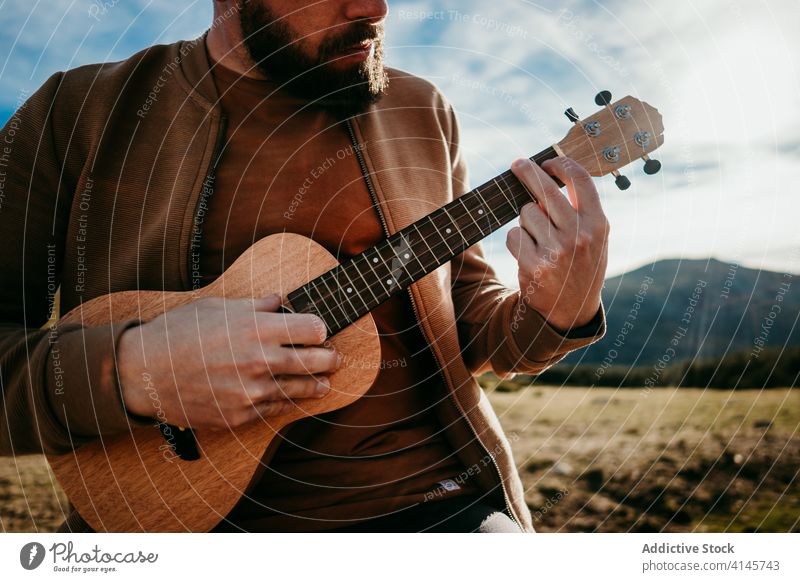 Anonymous bearded man playing ukulele in countryside fence sky cloudy music puerto de la morcuera spain male travel vacation trip nature rest journey sunny
